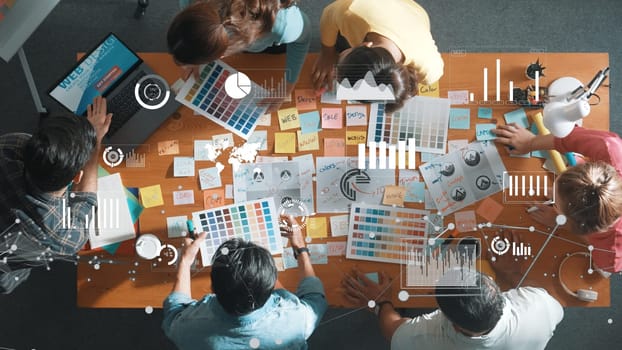 Top down view of business team with casual outfit looking laptop screen and sharing idea. Aerial view of manager works and checking color palette at table with statistic graph holographic. Symposium.