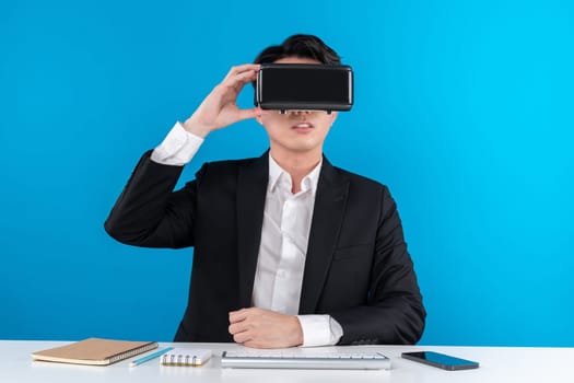 Asian businessman looking thorough VR connecting metaverse analyzing business world news in futuristic metaverse, analyzing innovation technology virtual reality isolated blue copyspace. Contrivance.