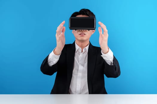 Asian businessman looking through VR connecting holding data object in air analyzing business futuristic metaverse innovation technology news virtual reality in isolated blue copyspace. Contrivance.