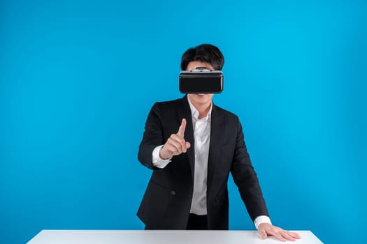 Asian businessman looking through VR connecting meta standing to hold hologram object on table in futuristic business metaverse innovation technology virtual reality in blue copyspace. Contrivance.