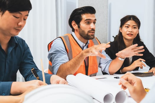 Diverse group of civil engineer and client working together on architectural project, reviewing construction plan and building blueprint at meeting table. Prudent