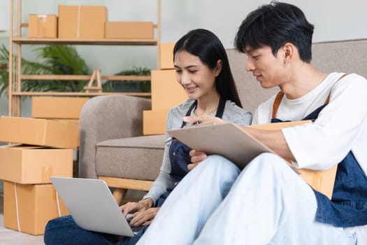 A couple working together to manage online orders and pack products for their e-commerce business from home, surrounded by boxes and a laptop.