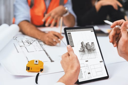 Diverse group of civil engineer and client working together on architectural project, reviewing construction plan and building blueprint using tablet at meeting table. Prudent