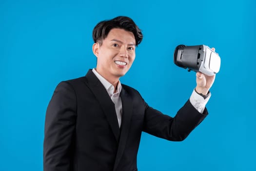 Asian businessman looking at camera holding VR connecting to financial report in futuristic metaverse business data analytics communication technology virtual reality in blue copyspace. Contrivance.