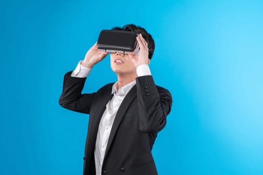 Smiling Asian businessman looking thorough VR connecting to business world report in futuristic metaverse, analyzing innovation technology ads in virtual reality isolated blue copyspace. Contrivance.