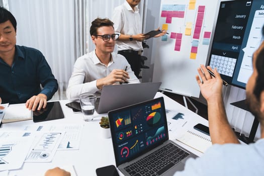 Project manager communicate and collaborate with team using project management software display on monitor, tracking progress of project task and making schedule plan at meeting table. Prudent