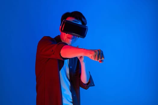 Smart Asian boxing gamer wearing VR playing boxer game to punch camera posing isolated blue neon light wall connected futuristic technology virtual reality in meta fighting box stadium. Contrivance.