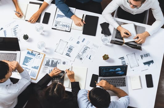 Top view analyst team utilizing BI Fintech to analyze financial data at table in meeting room. Analytic BI dashboard power on paper for business insight and strategic marketing planning. Prudent