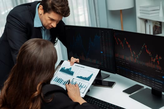 Two business traders discussing value business statistic graph company on paper report analyzing with dynamic stock exchange market currency real time website surround pc screens at office. Postulate.