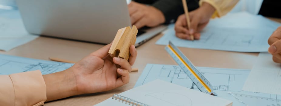 Professional architect team discussion about architectural project on meeting table with blueprint and wooden block scatter around at modern office. Closeup. Focus on hand. Delineation.