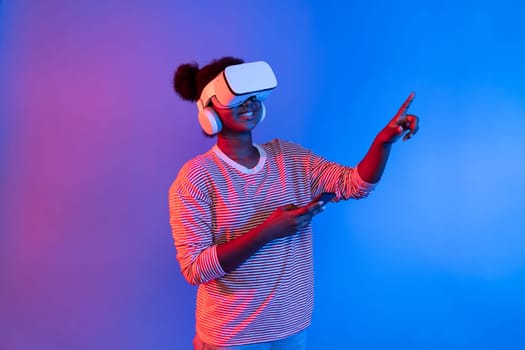 Surprised young African woman with VR headset and smartphone turing to metaverse with vibrant neon lighting background virtual reality and mobile connectivity learning online technology. Contrivance.