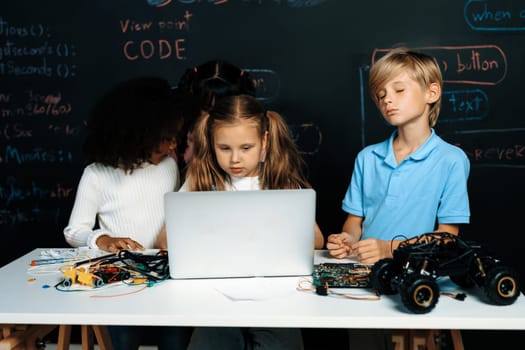Smart girl in white bib learning about coding robotics technology using laptop in the STEM class. Schoolboy in blue shirt try to educate motherboard while smart schoolgirls reading code. Erudition.