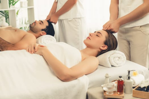 Caucasian couple enjoying relaxing anti-stress head massage and pampering facial beauty skin recreation leisure in dayspa modern light ambient at luxury resort or hotel spa salon. Quiescent
