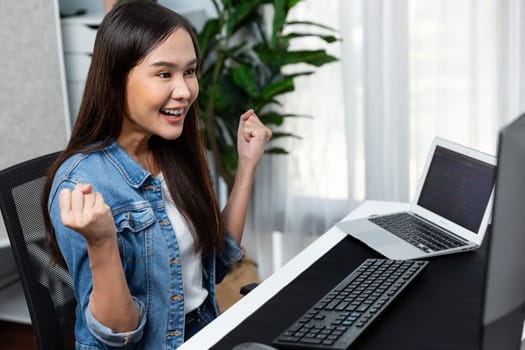 Smiling young Asian IT developer with happy face getting new software development information project with customer looking on pc screens, creating program coding to test at home office. Stratagem.