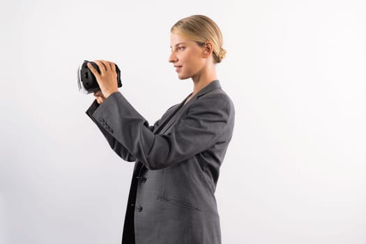 Caucasian business woman holding VR glass while standing at white background. Professional project manager looking visual reality goggle while wearing suit. Innovation technology concept. Contraption.