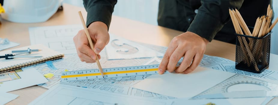 Professional engineer measuring the blueprint. Professional engineer working architectural project at studio on a table with yellow helmet and architectural equipment scatter around. Delineation.