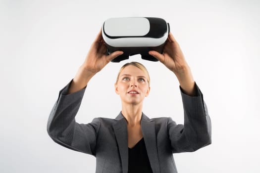 Caucasian business woman holding VR glass while standing at white background. Professional project manager looking visual reality goggle while wearing suit. Innovation technology concept. Contraption.