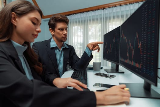 Two business traders discussing on dynamic stock market in currency rate investment trading on two pc screens with compare real time graph on risk or profit point of data at modern office. Postulate.