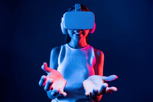 Smart Female standing surrounded by neon light wear VR headset connecting metaverse, futuristic cyberspace community technology, using both hands interact with generated virtual object. Hallucination.