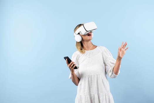 Caucasian girl wearing VR glasses while holding phone and pointing at view. Happy woman surprised while looking around to explore visual reality world or metaverse. Technology innovation. Contraption.