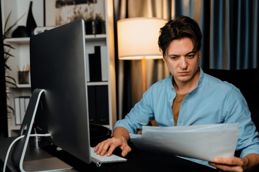 Smart businessman typing with keyboard on monitor with business paragraph dynamic data marketing analysis planning sheet aligning on report paperwork at modern home office at night time. Pecuniary.