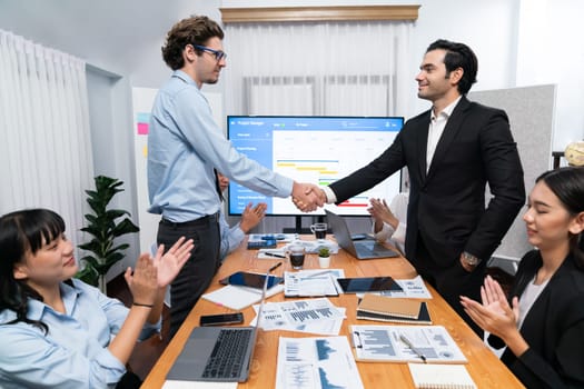 Cheerful meeting room, businesspeople celebrate with handshaking. Successful project was completed before the deadline. Business partnership and collaboration in project management. Habiliment