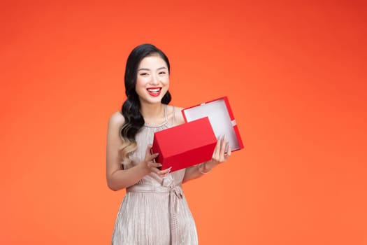 Portrait of a happy smiling girl opening a gift box isolated over red background