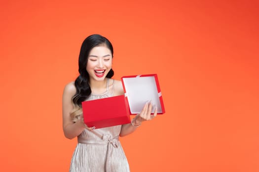 Portrait of beautiful young woman posing, opening present box over red background. 