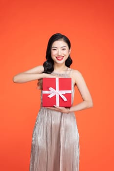 Cheerful attractive young woman holding gift boxes over red background