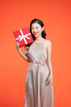 Young woman wearing a shiny dress holding a red gift box in front of a red backdrop