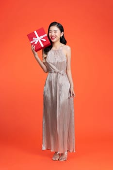 Cheerful attractive young woman holding gift boxes over red background