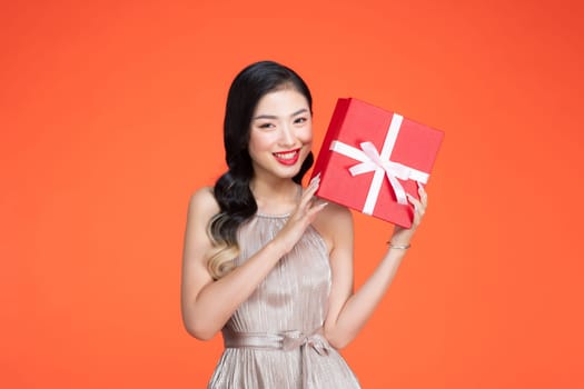 Portrait of happy girl shaking gift box wondering what inside as celebrating presents on red background