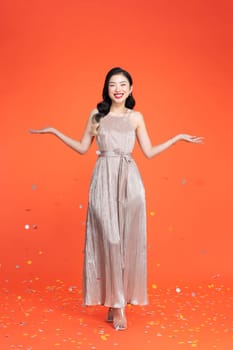 Portrait of beautiful smiling girl in shiny pink dress throwing confetti on red background. 