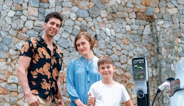 Family road trip vacation with electric vehicle, lovely family recharge EV car with green and clean energy. Stone seawall background and eco friendly car travel for sustainable environment. Perpetual