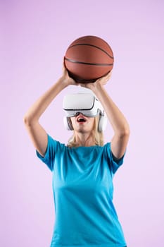 Girl wearing visual reality glasses and casual cloth and holding basketball. Caucasian woman playing basketball while standing at pink background at sport arena hologram. Innovation. Contraption.