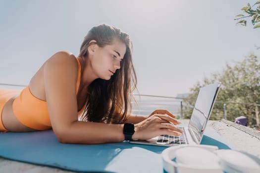 Digital nomad, Business woman working on laptop by the sea. Pretty lady typing on computer by the sea at sunset, makes a business transaction online from a distance. Freelance, remote work on vacation