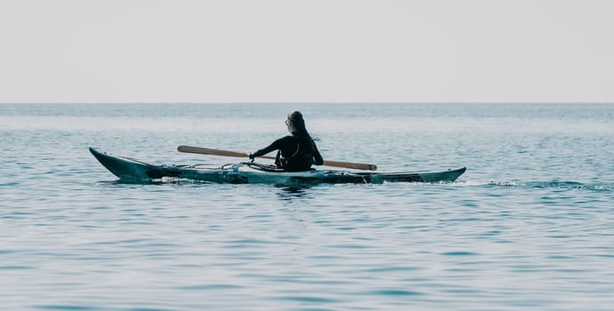 Happy smiling woman in kayak on ocean, paddling with wooden oar. Calm sea water and horizon in background