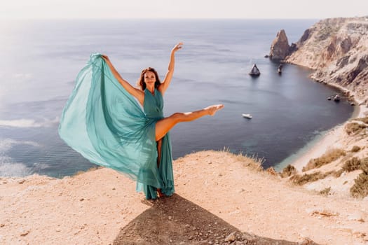 Woman green dress sea. Female dancer posing on a rocky outcrop high above the sea. Girl on the nature on blue sky background. Fashion photo