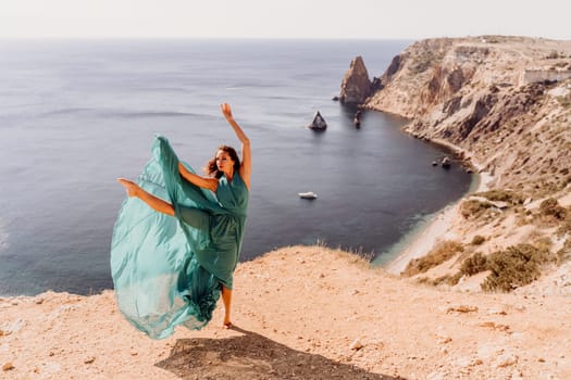 Woman green dress sea. Female dancer posing on a rocky outcrop high above the sea. Girl on the nature on blue sky background. Fashion photo