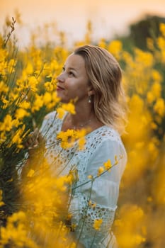 A woman is standing in a field of yellow flowers. She is wearing a white shirt and has her hair pulled back. The flowers are in full bloom, creating a bright and cheerful atmosphere