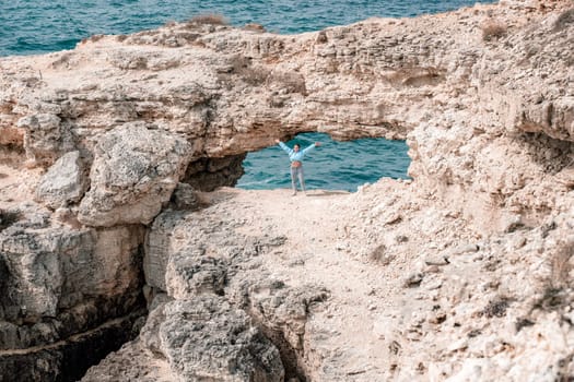 A woman stands in front of a large rock formation with her arms outstretched. Concept of freedom and adventure, as the woman is embracing the natural beauty of the rocky landscape