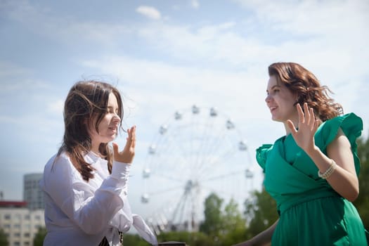 Happy Girls Enjoying Summer Day Together in the Park. Two young women stand on a platform in a park under a bright summer sky, smiling and relaxed