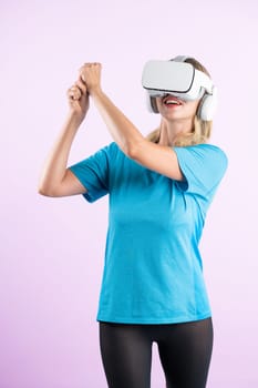 Caucasian girl playing golf and moving gesture by using VR glasses. Happy sport gamer with casual cloth playing game while wearing visual reality headset and standing at pink background. Contraption.