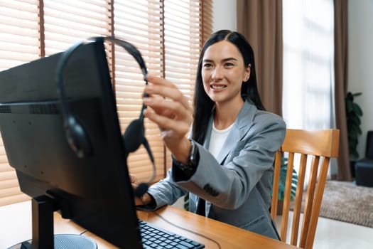 Female call center operator or customer service helpdesk staff working on workspace while talking on the headset to provide assistance for customer. Professional modern business service. Blithe