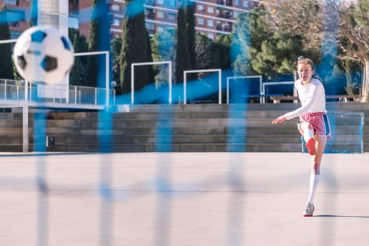 female football player kicking a soccer ball into the goal on an urban field, concept of sport and active lifestyle, copy space for text