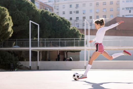 young caucasian woman kicking a soccer ball on an urban field, concept of sport and football lifestyle, copy space for text