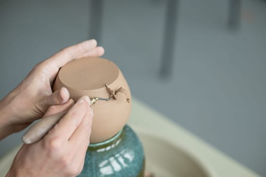 A potter works with a tool on a potter's wheel. Close-up of a man's hands