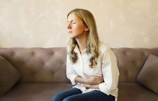 Young woman put hands on abdomen suffering from stomach ache griping bellyache feel bad with pain sitting on a couch at home