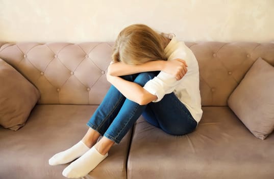 Upset sad crying woman covering her eyes and face with her hands while experiencing mental or physical suffering, fatigue sitting on the couch in room at home