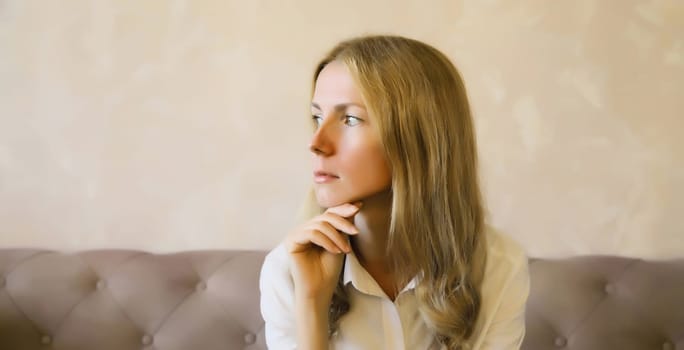 Pensive young woman thinks looks out the window, thoughtful girl suffering from depression sitting on the couch in living room at home